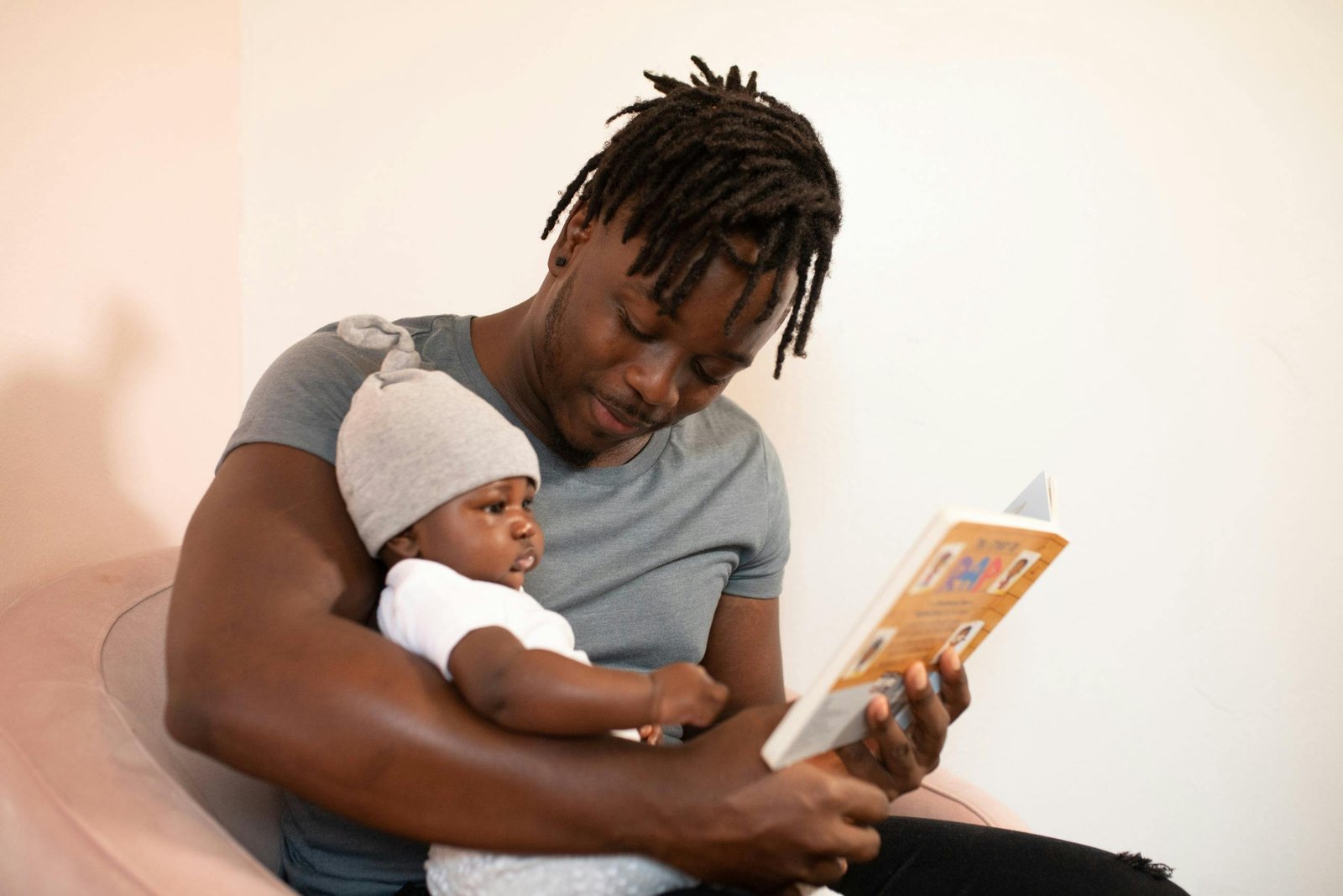 pexels-photo-3536630-3536630 A father with dreadlocks reads a book to his baby, creating a bonding moment.